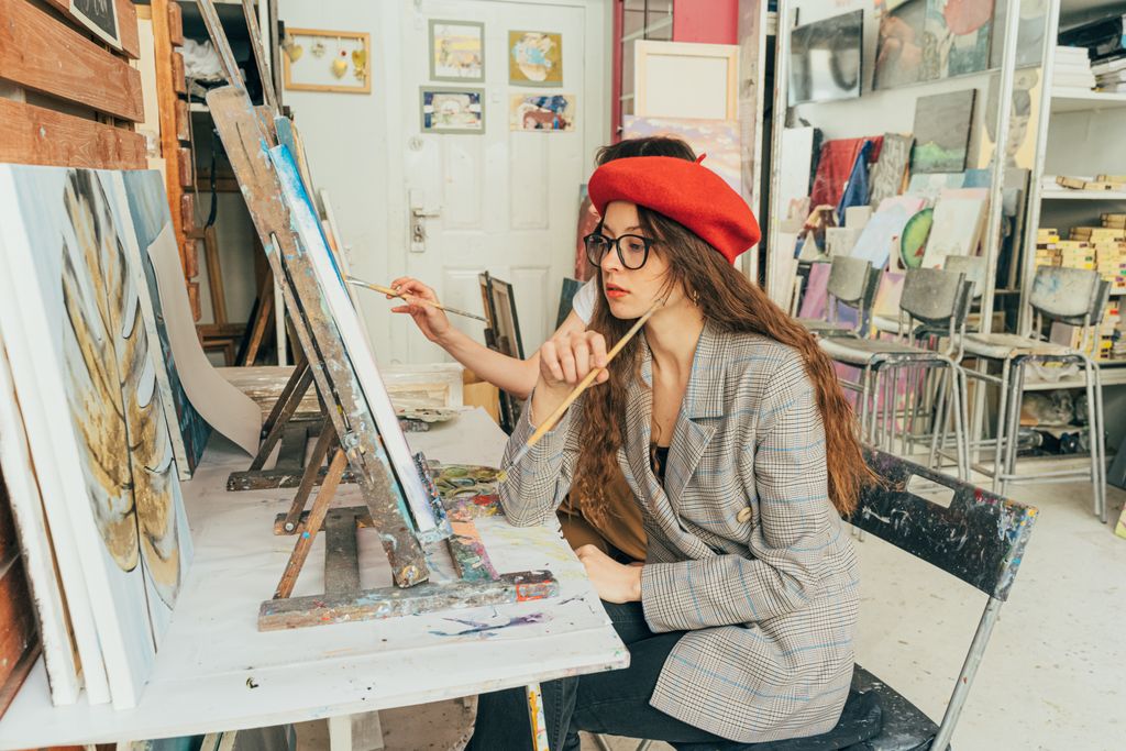 A young artist in a red beret paints attentively in an art studio full of canvases and supplies.