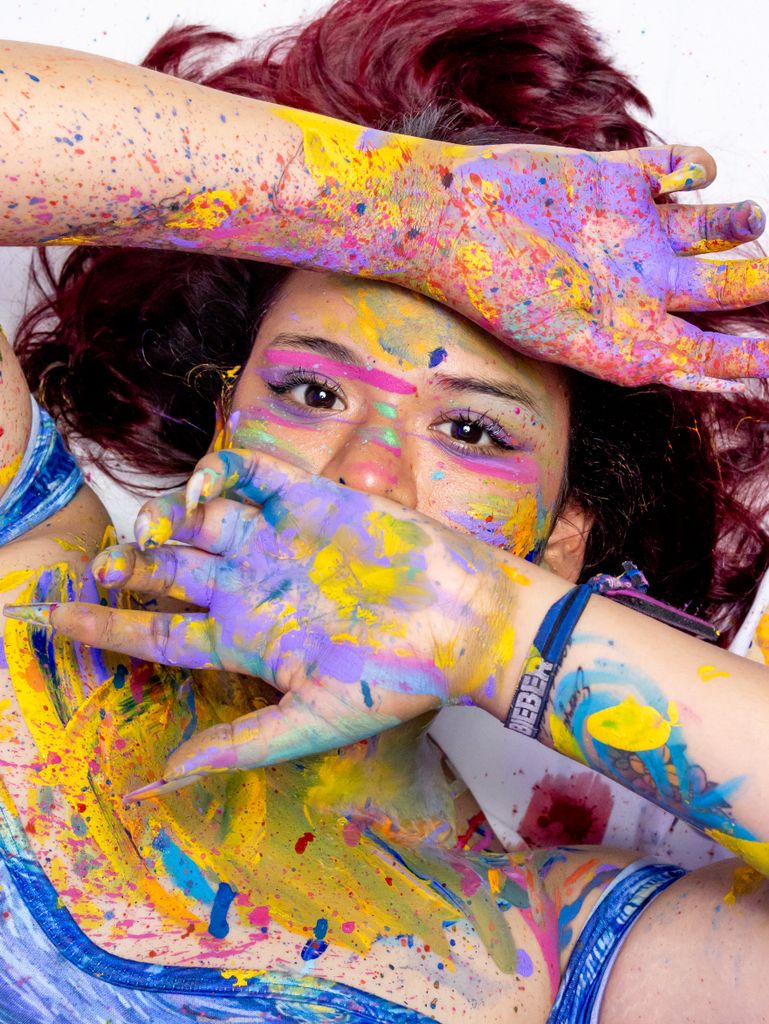 A young woman joyfully engaged in creative color splatter art, embodying fun and expression.