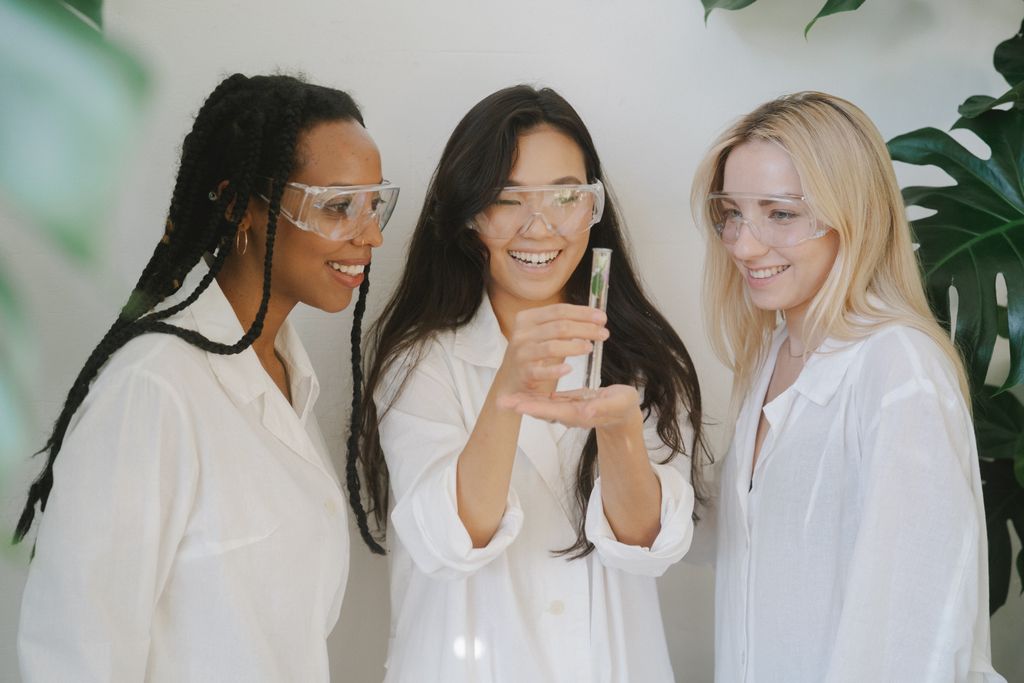 Three diverse female scientists smiling and examining a test tube in a laboratory setting.